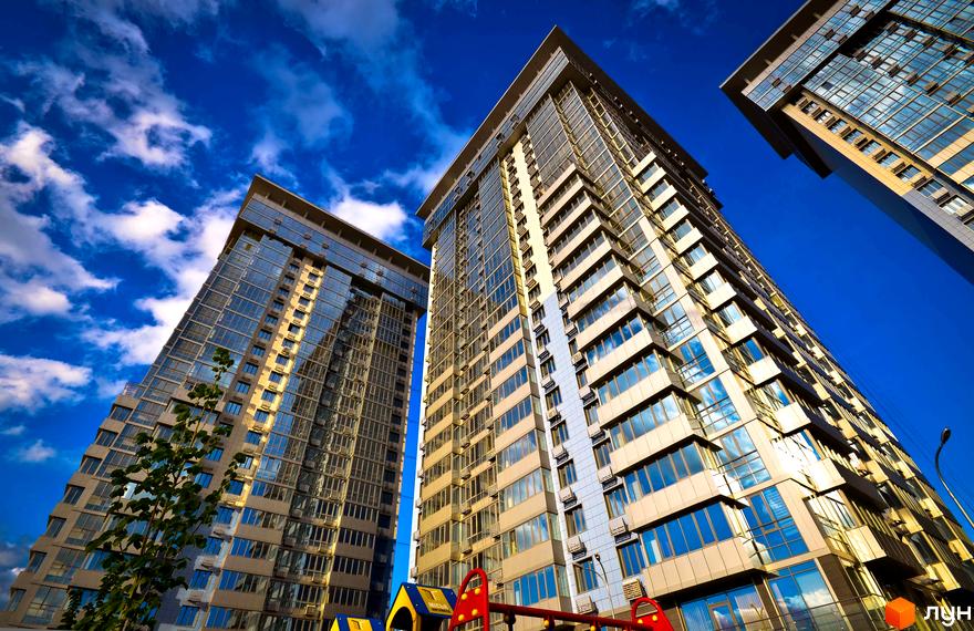 Високі житлові будинки Житлового комплексу RiverStone з вікнами, що відображають блакитне небо. На передньому плані розташований дитячий майданчик.