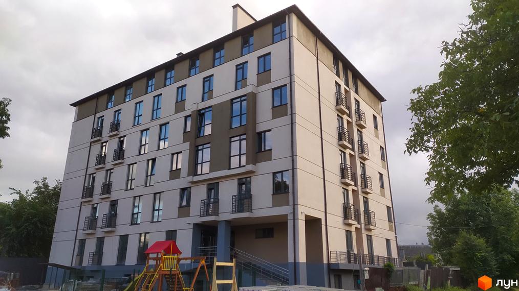 Зовнішній вигляд новобудови по вул. Василя Алексухіна, 24 з балконами та вікнами. Поруч дитячий майданчик.