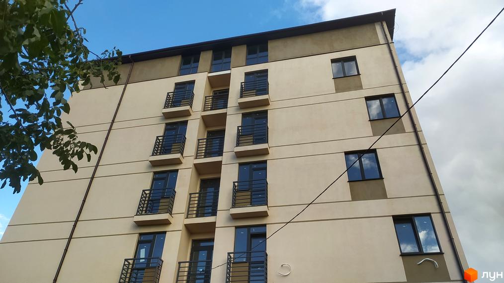 Фасад новобудови на вул. Василя Алексухіна, 24, з численними балконами та вікнами на тлі блакитного неба з хмарами.