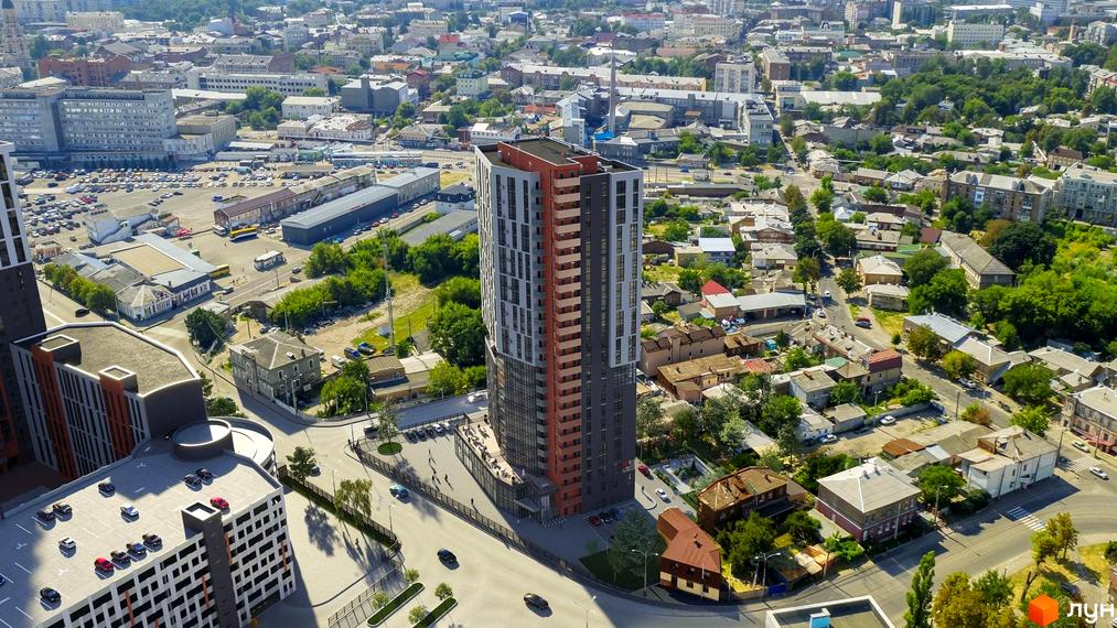 Вид на новобудову ЖК BonAparte з фасадом з сірих та червоних панелей, з прибудинковою територією та парковкою.