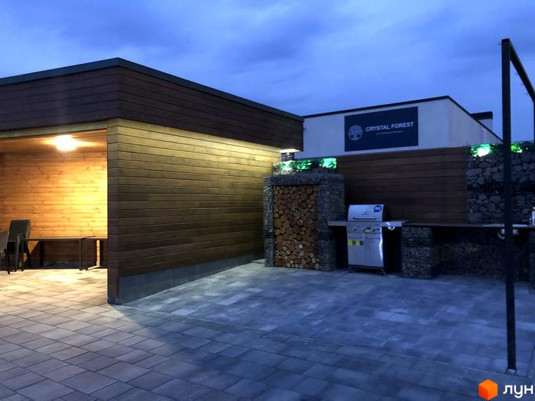 Зовнішній вигляд будинку КМ Crystal Forest з терасою та зоною барбекю. Панорамний вид на прибудинкову територію з бруківкою.