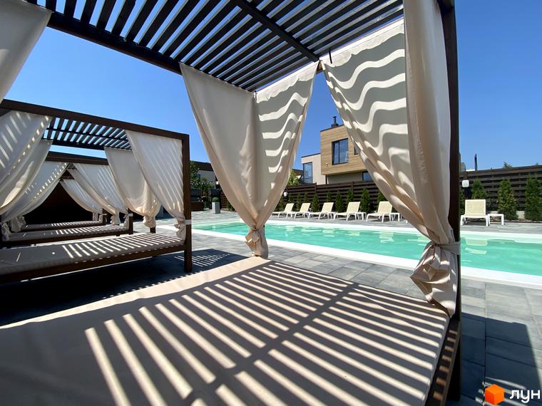 Котеджне містечко Crystal Forest. Територія з басейном та лежаками, обладнаними навісами з тканини для відпочинку.