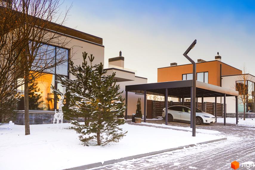 Зимовий вигляд будинку в Котеджному містечку Crystal Forest. На території сніг, росте ялинка, поруч критий паркінг для авто.