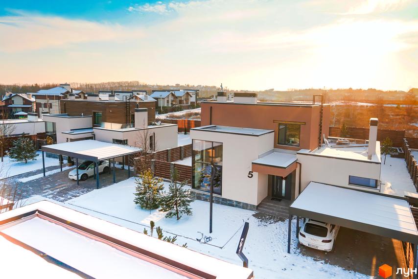 Зимовий краєвид котеджного містечка Crystal Forest. Сучасні будинки з білими фасадами та гаражами-навісами, вкриті снігом. На території ростуть ялинки.