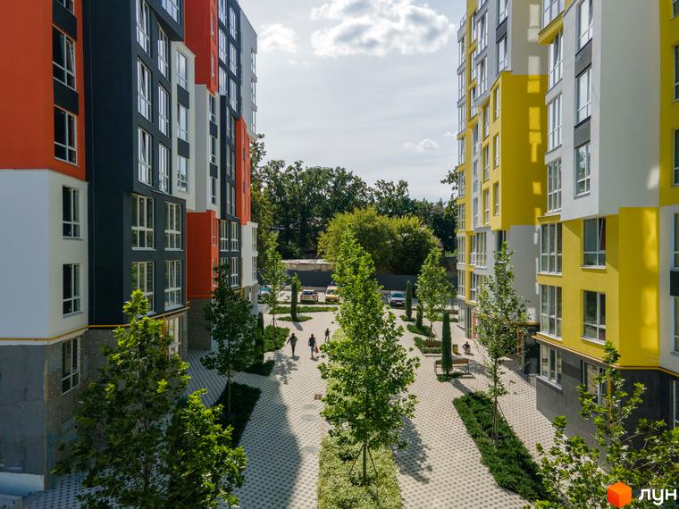 Житловий комплекс Синергія-3+ з яскравим фасадом та доглянутою прибудинковою територією. На території розташовані дерева та пішохідні доріжки.