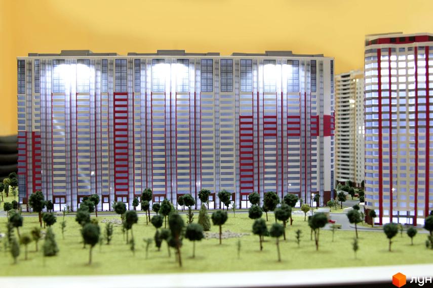 Модель житлового комплексу Позняки-4а з багатоповерховими будинками та червоно-білими фасадами. Навколо будівель розташована зелена прибудинкова територія з деревами.