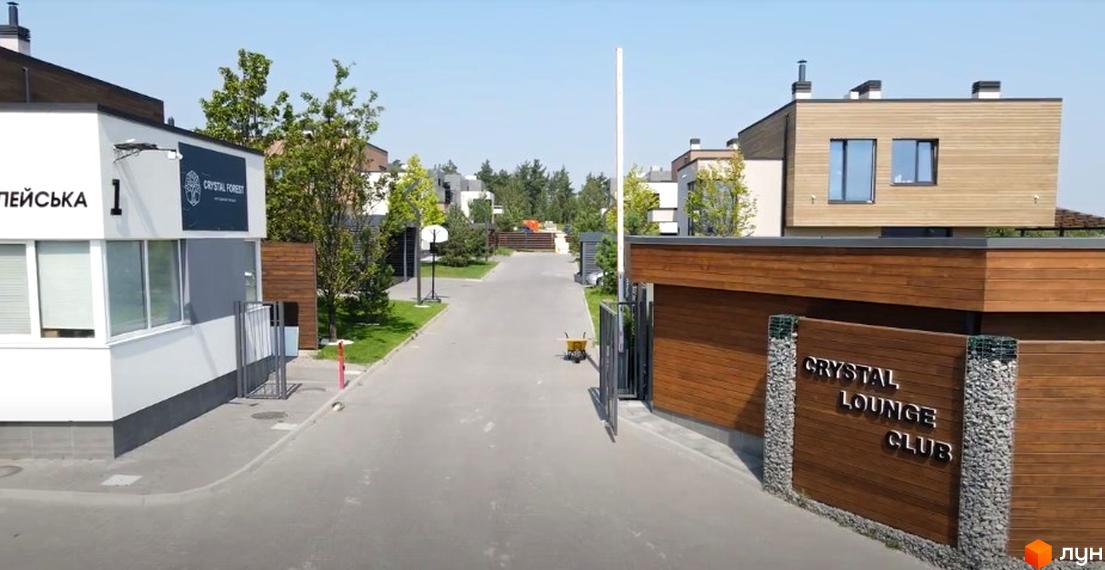 В'їзд до Містечко котеджів Crystal Forest. Огороджена територія з будинками з дерев'яним оздобленням та воротами. На території є дорога та зелені насадження.