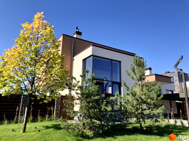 Будинок в Котеджному комплексі Crystal Forest з великими вікнами та світлими стінами. На території зелена трава та дерева.