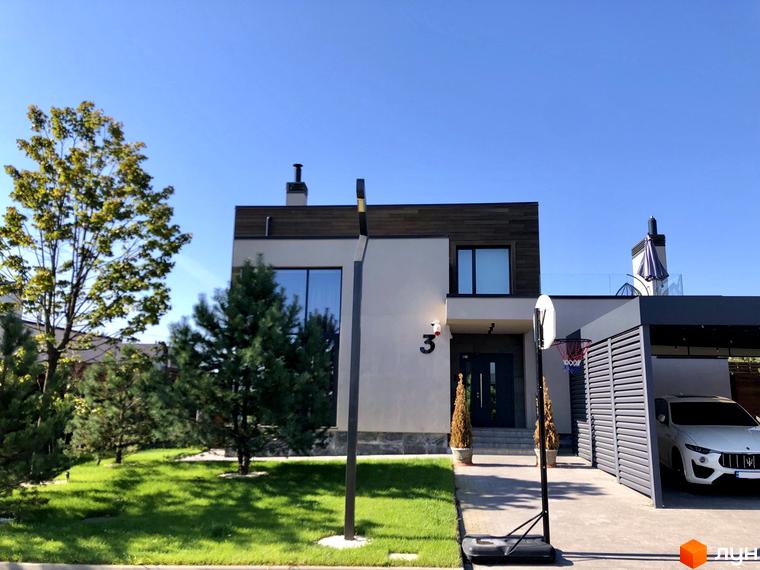 Зовнішній вигляд будинку в Котеджному містечку Crystal Forest. На передньому плані газон з деревами та баскетбольне кільце, поруч з будинком гараж з автомобілем.