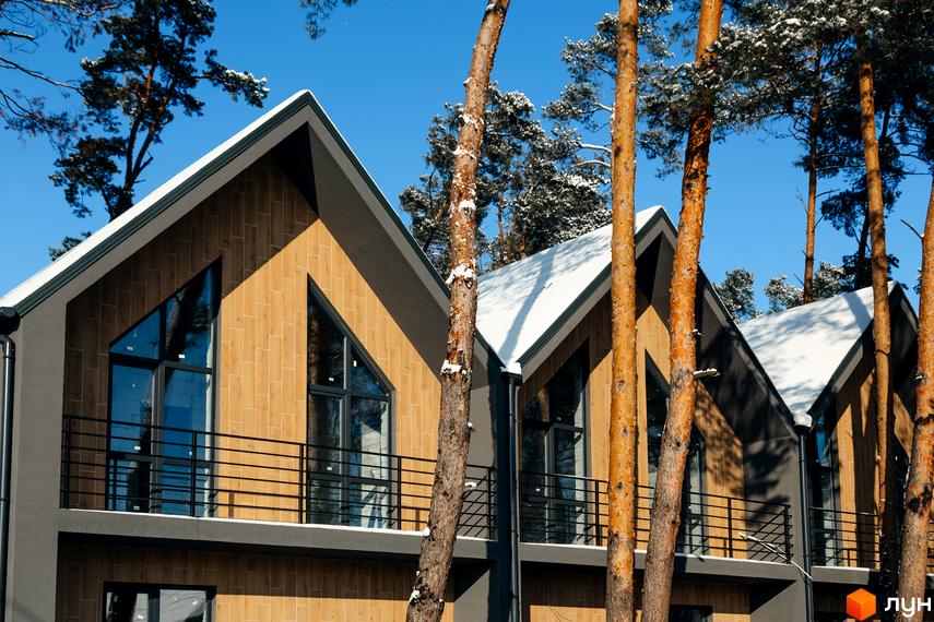 Таунхауси Positano-3 у зимовому лісі з трикутними вікнами та дерев'яним фасадом. Зовнішній вигляд новобудови з балконами та снігом на даху.