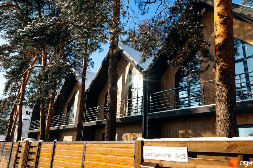 Зовнішній вигляд таунхаусів Positano-3 на тлі соснового лісу взимку. Дерев'яна огорожа на передньому плані.