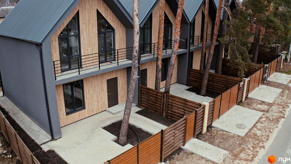 Таунхауси Positano-3 з дерев'яним фасадом та темним дахом, оточені соснами та огороджені дерев'яним парканом.