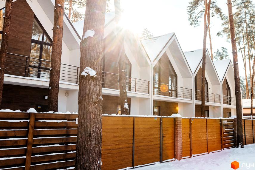 Ряд таунхаусів Таунхауси „Positano-2“ з білими фасадами, темними вікнами та снігом на дахах. Перед будинками видно дерев'яний паркан та засніжену територію з соснами.