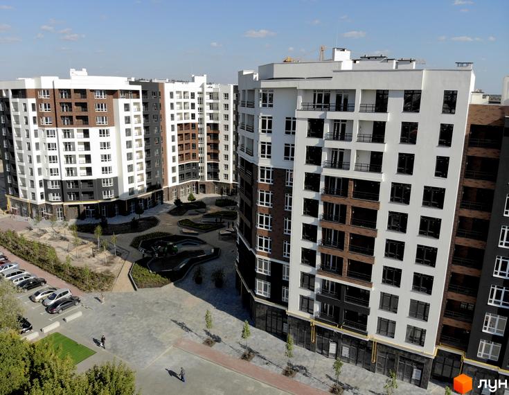 Житловий комплекс Синергія Сіті від Kvartal Group. Багатоповерхові будинки з білою, сірою та цегляною обробкою фасадів, упорядкована прибудинкова територія з зеленими зонами та паркуванням.