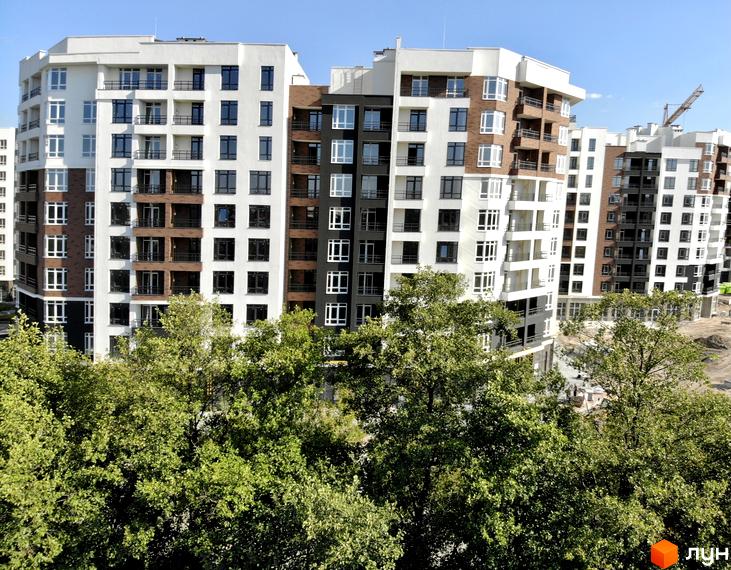 Новобудова ЖК Синергія Сіті від Kvartal Group з біло-коричневими фасадами та численними вікнами, оточена зеленими деревами.