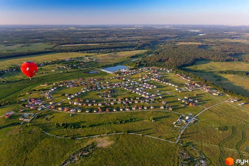 Вид з повітря на котеджне містечко КМ Home Resort з червоним повітряною кулею. Забудова розташована серед зелених полів та лісів.