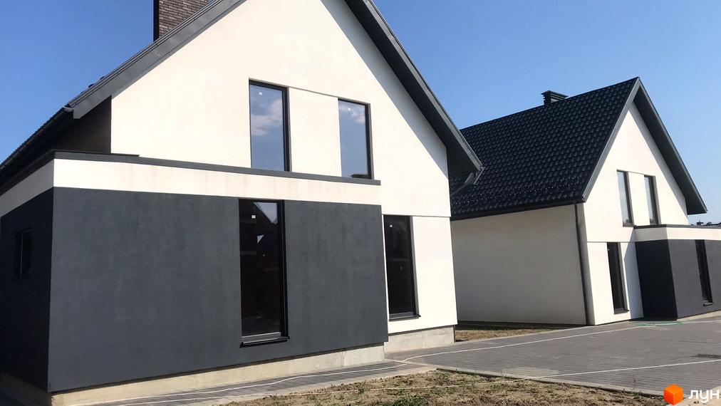 Двоповерхові будинки з білими стінами та темними вікнами. На території є тротуарна плитка та невеликий газон.