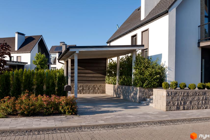 Котеджне містечко КМ VILLAGGO. Зовнішній вигляд білого будинку з навісом для авто та доглянутою прибудинковою територією з туями та кущами.