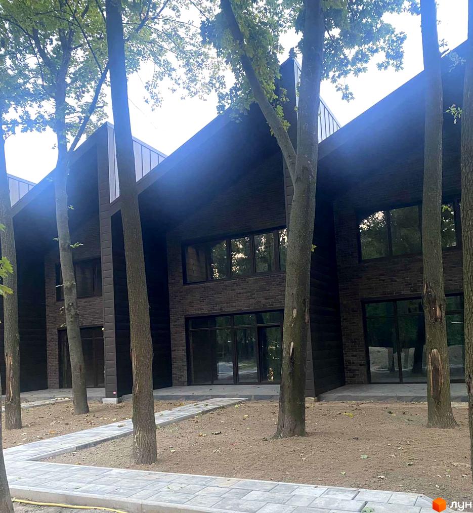 Таунхаус Forest Park Gora з темним фасадом та великими вікнами, оточений деревами та вимощеними доріжками.