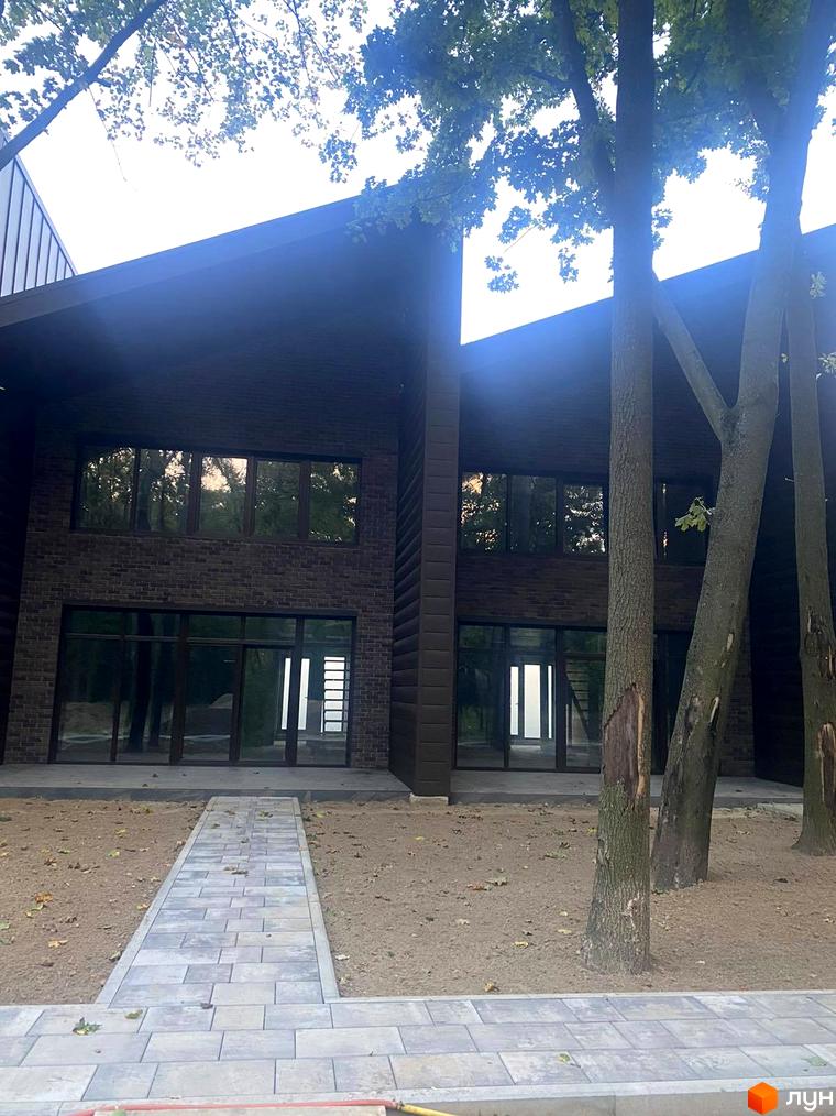 Таунхаус Forest Park Hora - новобудова з темної цегли та великими вікнами, оточена деревами та вимощеною доріжкою.