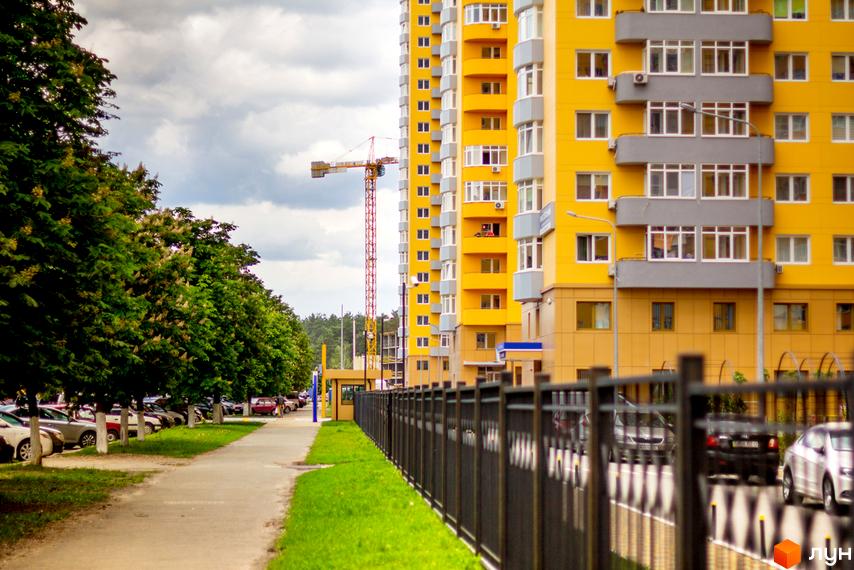 Житловий комплекс на Кондратюка з жовтою фасадною обробкою та прибудинковою територією, озелененою деревами.