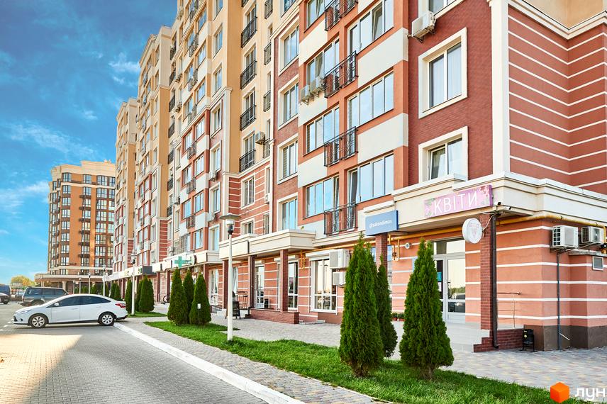 Зовнішній вигляд новобудови ЖК Нові Теремки з цегляним фасадом та балконами. Прибудинкова територія з зеленими насадженнями та парковкою.