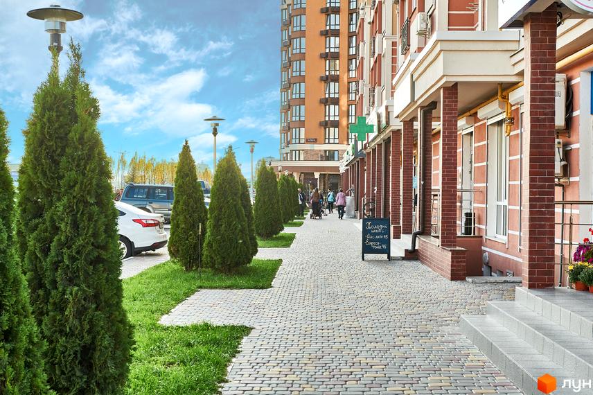 Житловий комплекс Нові Теремки: фасади будинків з цегляним оздобленням та доглянута прибудинкова територія з зеленими насадженнями та бруківкою.