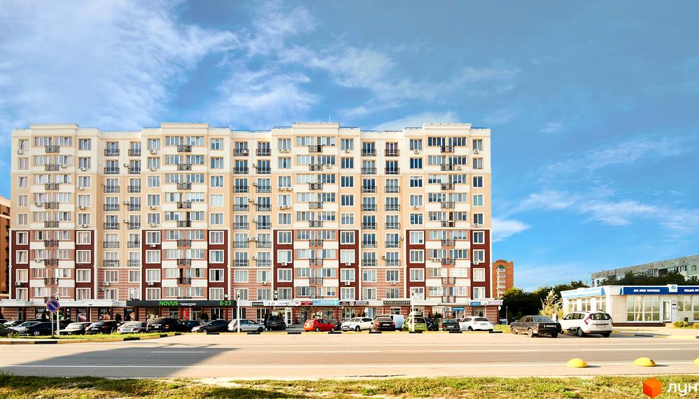 Житловий комплекс Нові Теремки: багатоповерховий будинок світлих кольорів з балконами, перед яким парковка та магазини.