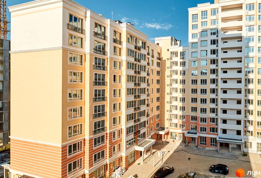 Житловий комплекс Нові Теремки: світлі багатоповерхові будинки з помаранчевими акцентами та внутрішній двір з автомобілями.