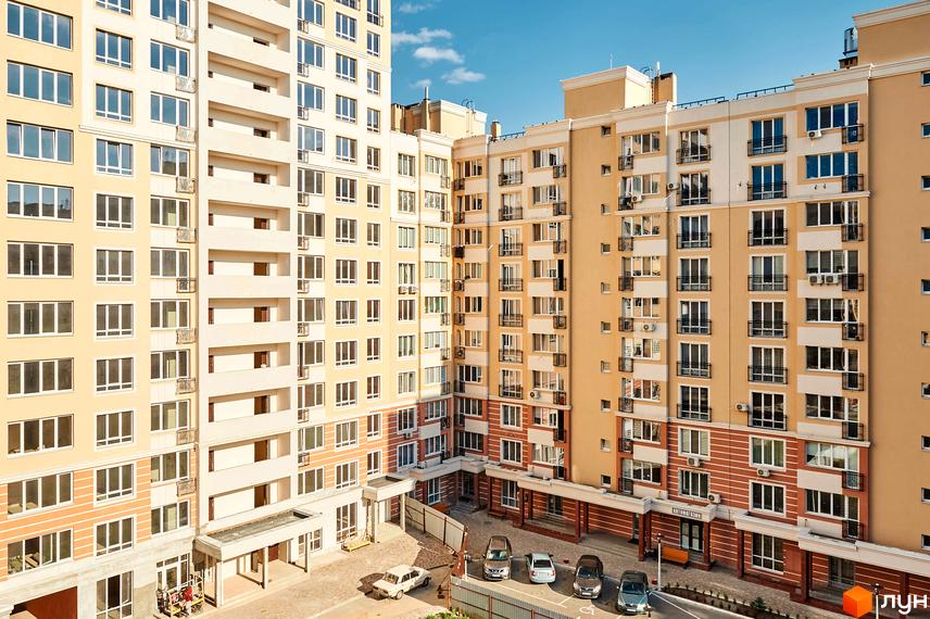 Житловий комплекс Нові Теремки: багатоповерхові будинки світлого кольору з балконами та великими вікнами. На прибудинковій території видно парковку та входи до під'їздів.