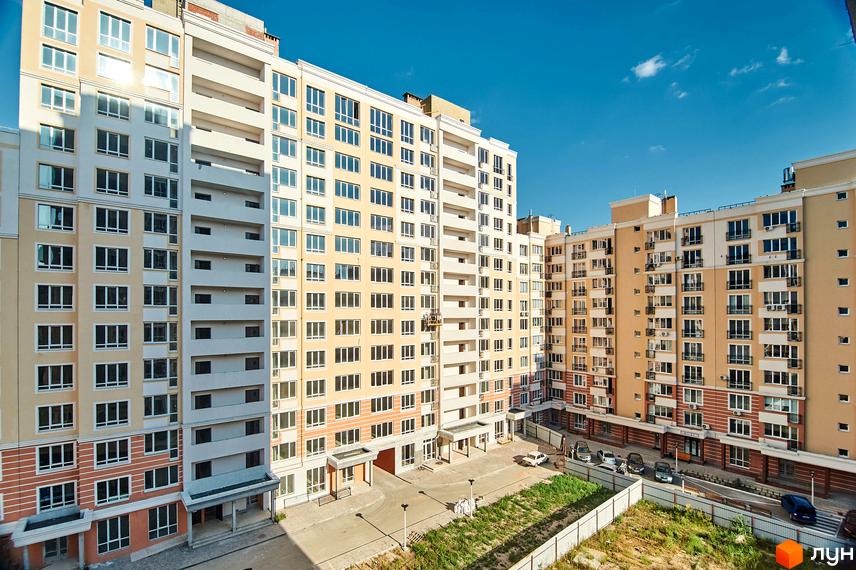 Зображення фасаду та прибудинкової території Житлового комплексу Нові Теремки. Багатоповерхові будинки з великою кількістю вікон, двір з газоном та паркінгом.