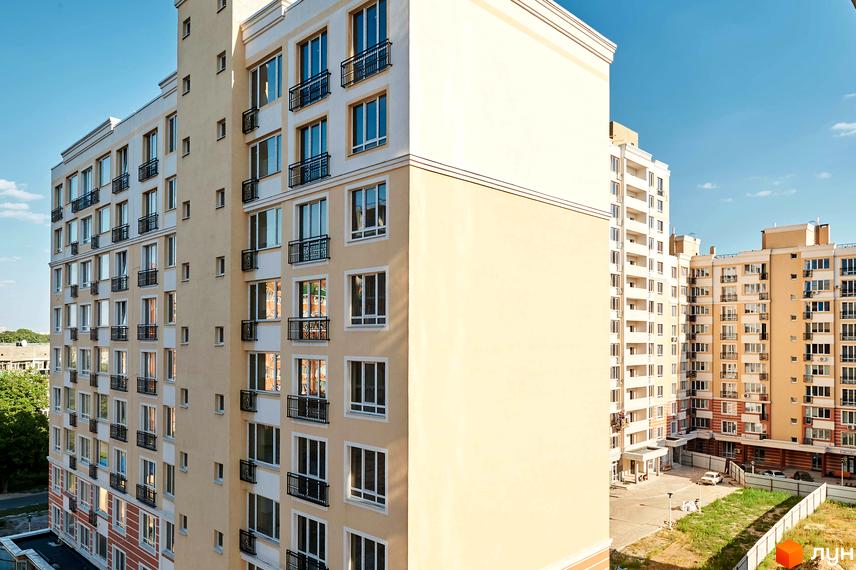 Зображення фасаду багатоповерхового будинку в Житловому районі Нові Теремки. Вигляд новобудови з вікнами та балконами на тлі блакитного неба.