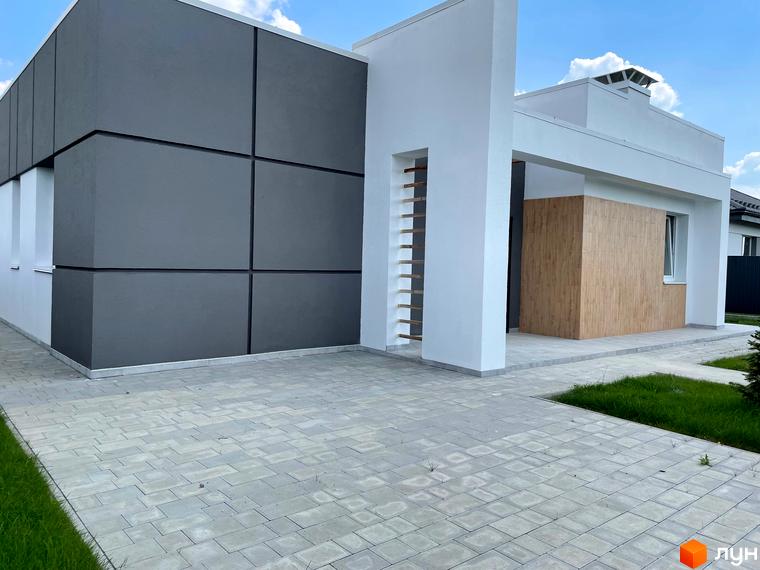 Зовнішній вигляд будинку КМ Лісне: сіра та біла фасадна обробка, дерев'яні вставки. Прибудинкова територія з бруківкою та зеленню.