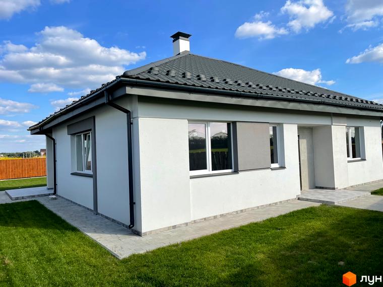 Котеджне містечко КМ Лісне: одноповерховий будинок з сірим дахом та білими стінами, вікнами та ролетами. Прибудинкова територія з газоном та доріжками.