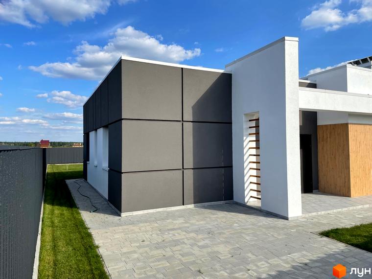 Зовнішній вигляд будинку КМ Лісне з сірими та білими фасадами та дерев'яними елементами. Прибудинкова територія з вимощеним подвір'ям та зеленою галявиною.