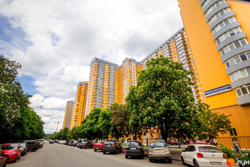 Житловий комплекс на Кондратюка, 5. Яскраві жовто-сірі багатоповерхівки з балконами. Парковка та зелені дерева біля будівель.
