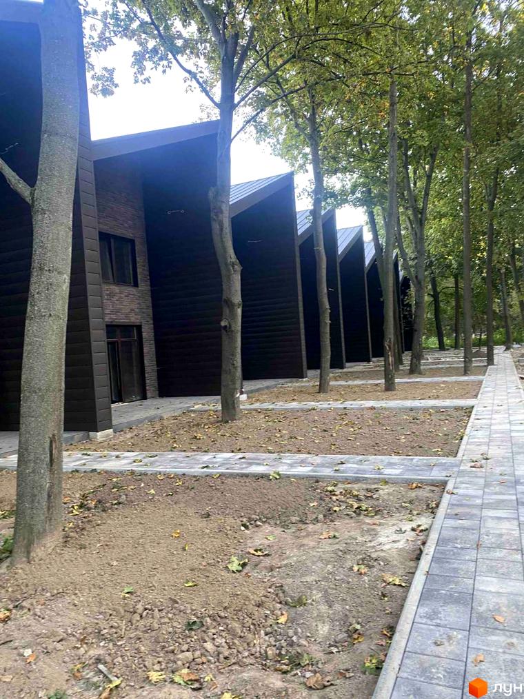 Таунхаус Forest Park Gora з темним фасадом та похилим дахом, розташований серед дерев із вимощеною доріжкою.