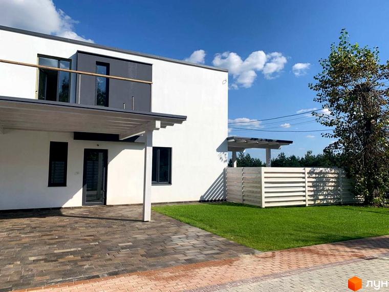 Котеджне містечко КМ Wood Side Village: двоповерховий білий будинок з темними вікнами та навісом, вимощена бруківкою тераса та зелений газон.