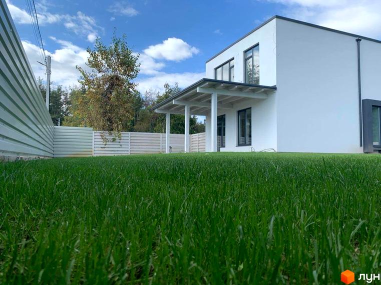 Котеджне містечко КМ Wood Side Village з білим фасадом та зеленою галявиною. Прибудинкова територія огороджена парканом.