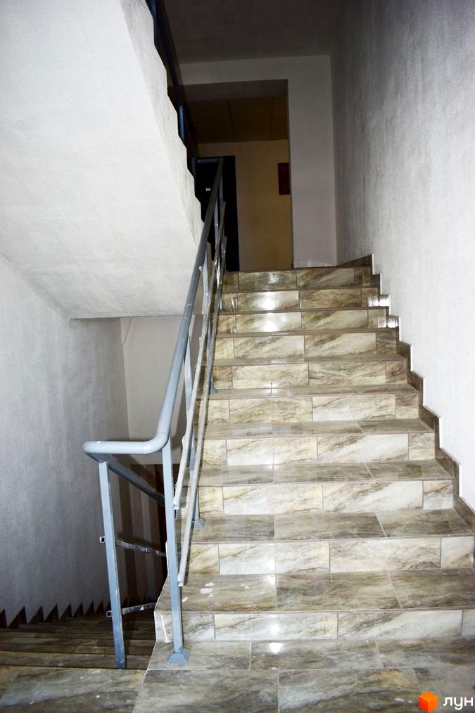 Сходи в підʼїзді ЖК Сузір'я 2020 з кахельною плиткою, металевими поручнями та дверима на верхньому поверсі.