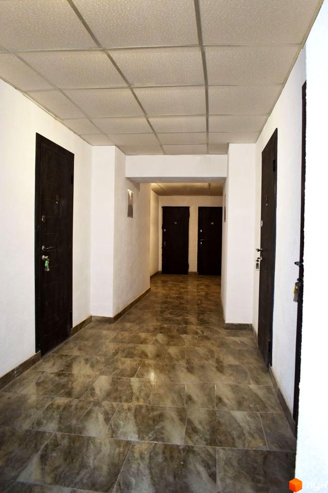 Коридор в новобудові. На стінах біла штукатурка, на підлозі плитка. Темні двері з номерами квартир.