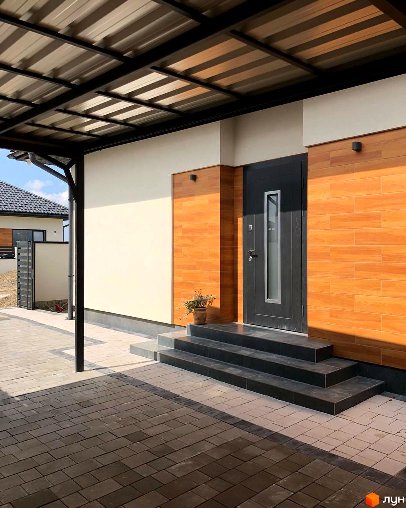 Вхідна група в Котеджному містечку HAPPY HOUSING з темними сходами та оздобленням фасаду деревом, бруківка на подвір'ї.