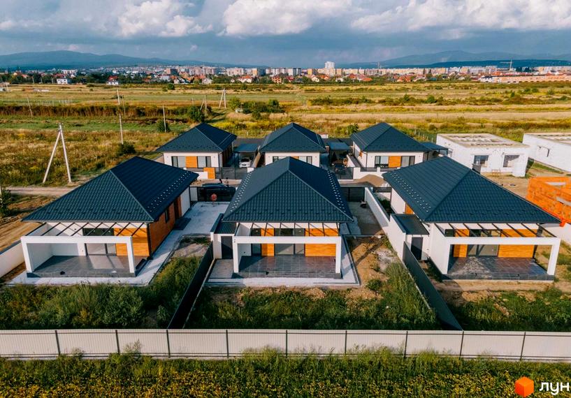 Котеджне містечко HAPPY HOUSING. Одноповерхові будинки з темною покрівлею та терасами, розташовані на зеленій прибудинковій території.