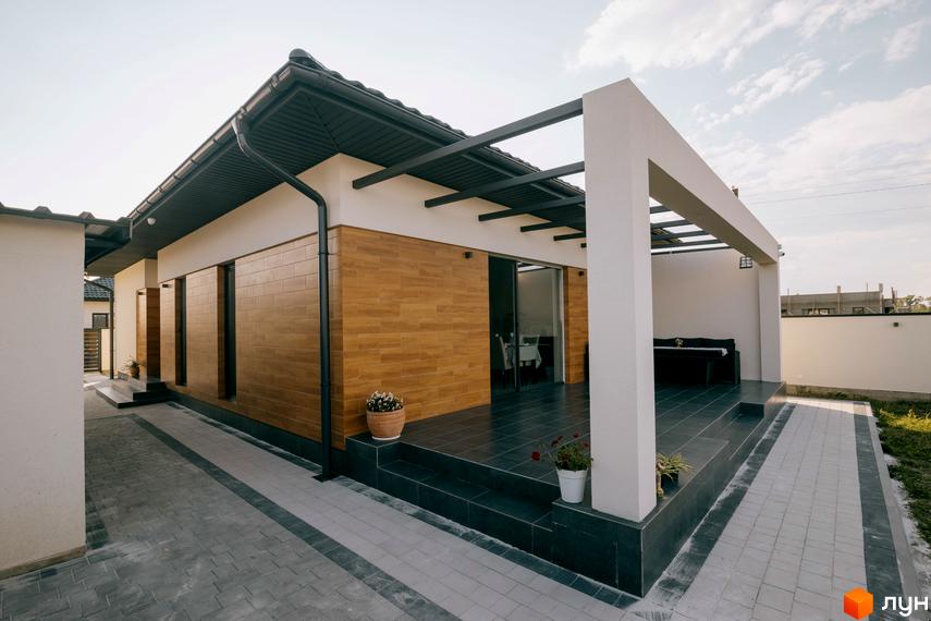 Одноповерховий будинок з терасою та панорамними вікнами в Котеджному комплексі HAPPY HOUSING. Доглянута прибудинкова територія з бруківкою та рослинами.