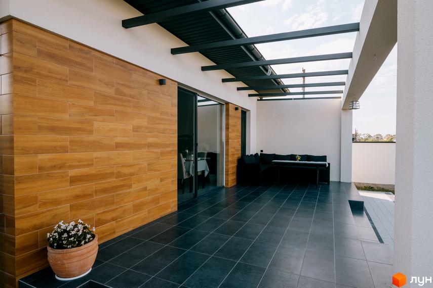 Тераса в будинку Котеджне містечко HAPPY HOUSING з дерев'яною обробкою стін, чорною плиткою на підлозі та м'якими меблями.