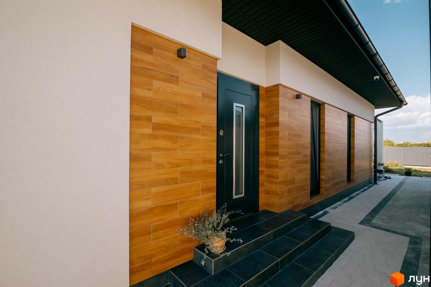 Вхідна група будинку в Котеджному містечку HAPPY HOUSING: чорні сходи, облицювання фасаду під дерево, біла стіна, газон та доріжка.