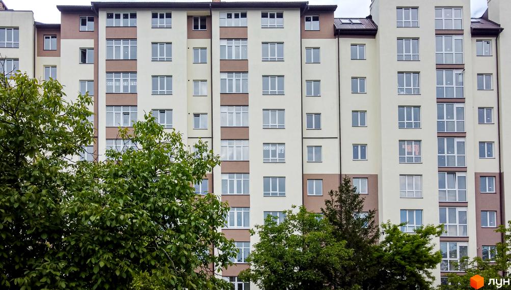 Фасад житлового комплексу Парковий маєток з численними вікнами та балконами, оточений зеленню дерев. Зовнішній вигляд новобудови, що демонструє архітектуру будинку.