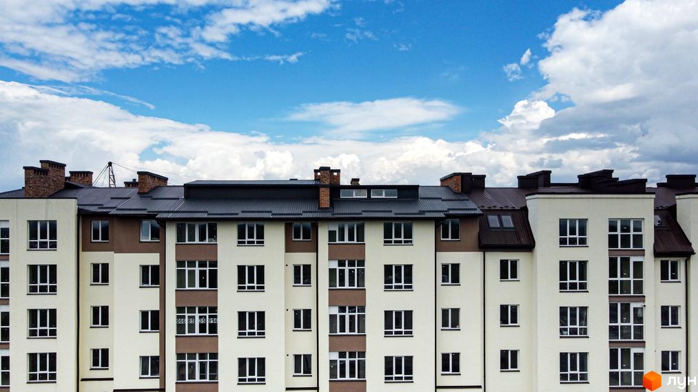 Зовнішній вигляд новобудови ЖК Парковий маєток з багатьма вікнами та коричневими елементами фасаду під блакитним небом з хмарами. Будівельний проєкт має багатоповерхові секції.