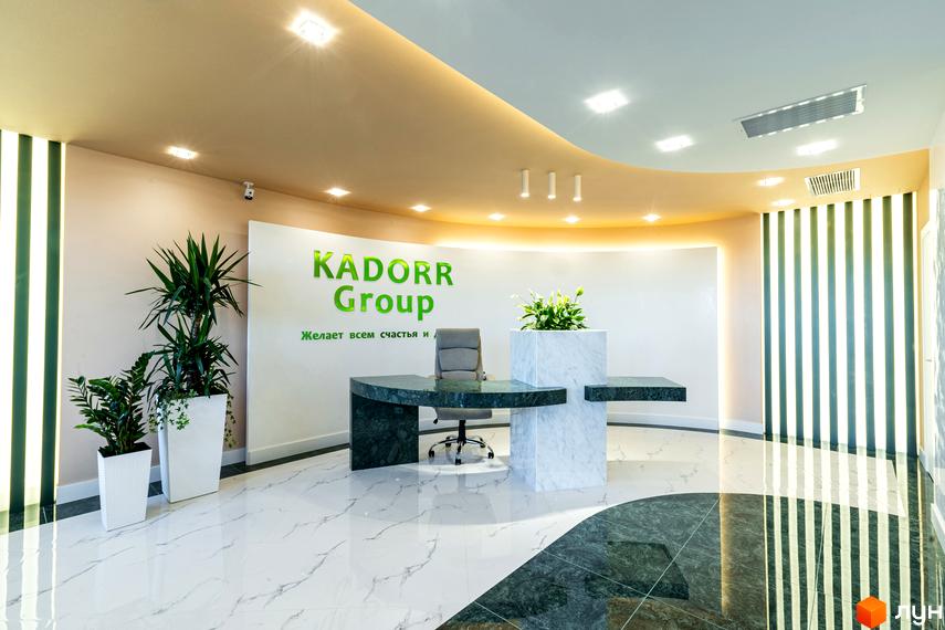 Сучасний інтер'єр рецепції житлового комплексу KADORR Group із зеленою вивіскою та мармуровими елементами.