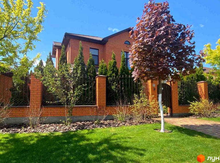 Котеджне містечко КМ Home Resort. Фасад цегляного будинку з червоної цегли, зелений газон та дерева на прибудинковій території.